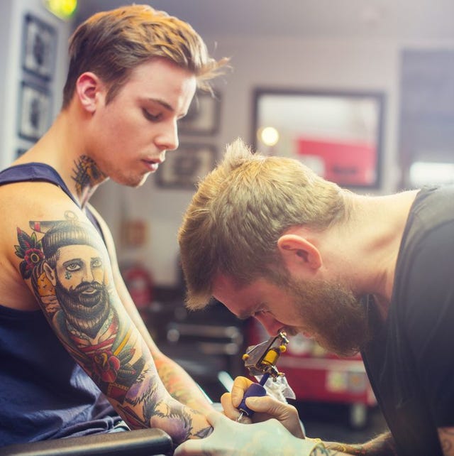 a photo of expert making tattoo on mans hand male customer looking at professional tattooing his hand tattoo artist is working in studio