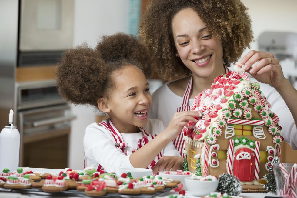 black mother and daughter decorating gingerbread house