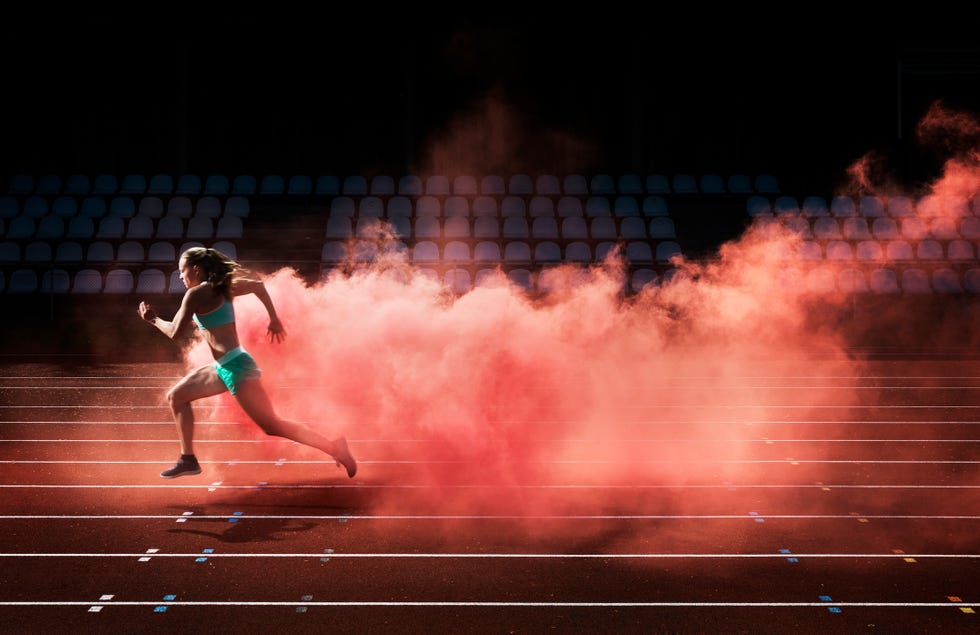 female athlete running in red smoke on stadium