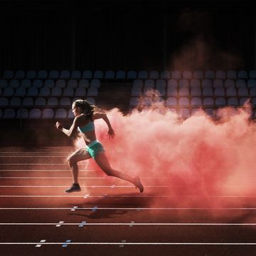 female athlete running in red smoke on stadium