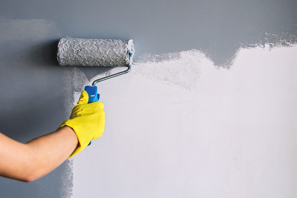 hand in yellow glove painting wall in gray color with a roller brush