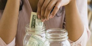 Mixed race woman putting money in savings jars