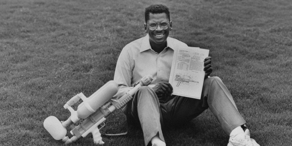 lonnie johnson holding a super soaker and its us patent while sitting on the grass outside his home, june 1992