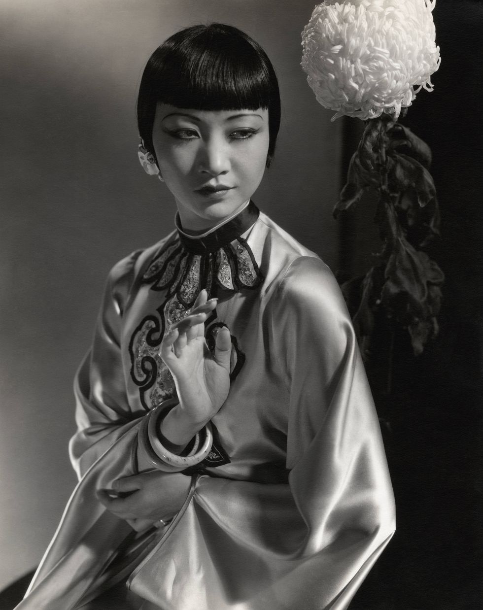 actress anna may wong wearing an embroidered chinese lounging robe in silk satin, and standing with a flower behind her left shoulder photo by edward steichencondé nast via getty images