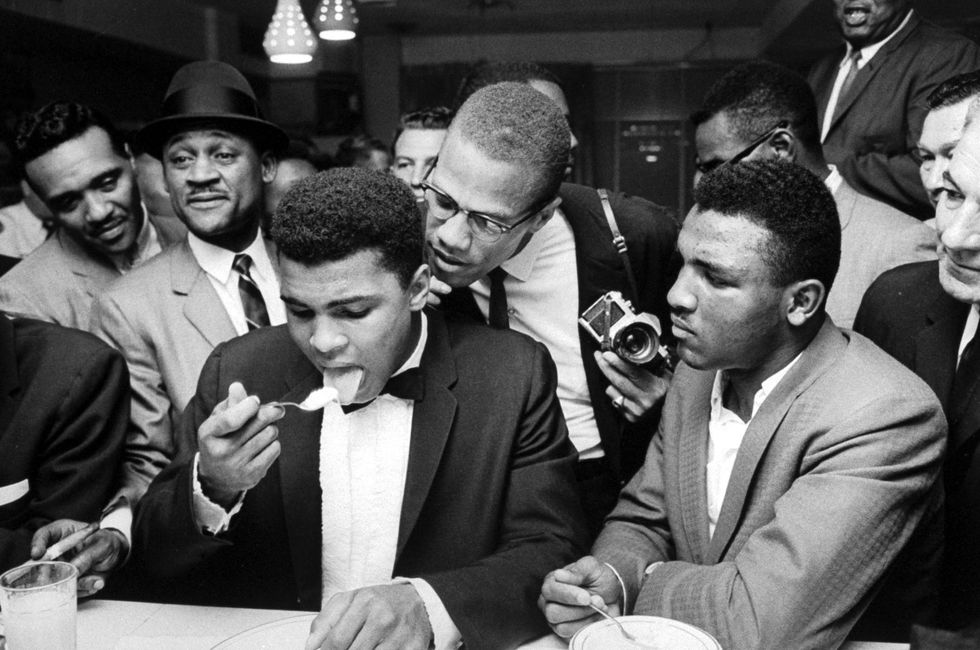 Malcolm X (C), standing behind tux-clad Muhammad Ali (L), who is surrounded by jubilant fans after he beat Sonny Liston for the heavyweight championship of the world.