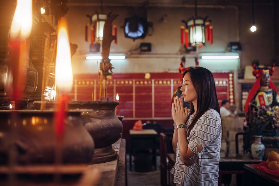 young asian female put her palms together praying sincerely and devoutly in a temple