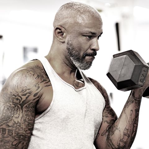Tätowierter bärtiger schwarzer Mann mittleren Alters, der in einem Fitnessstudio Gewichte hebt