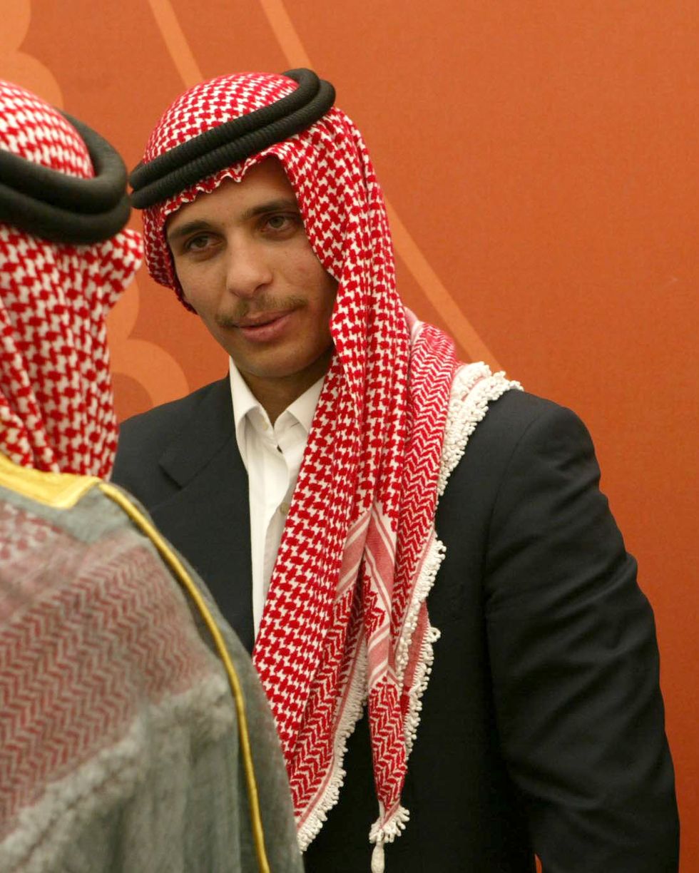 prince hamzah bin hussein of jordan talks with an unidentifiable person whose back is facing the camera, prince hamzah wears a dark suit jacket, white collared shirt and a red and white headscarf
