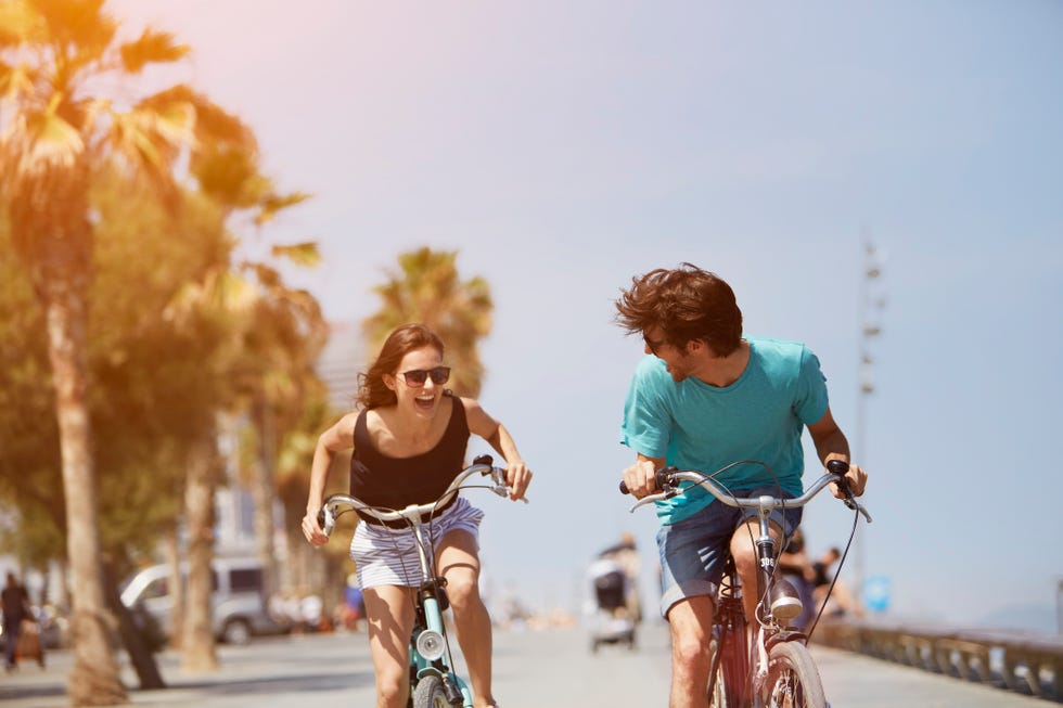 happy young woman chasing man while riding bicycle during summer vacation
