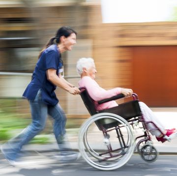 caregiver playfully pushing an elderly woman in her wheelchair outdoors in the grounds of the retirement home