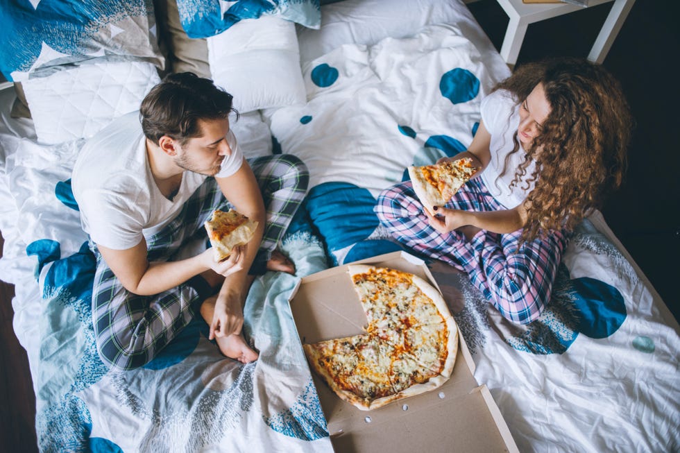 couple having pizza in the bed in bedroom.