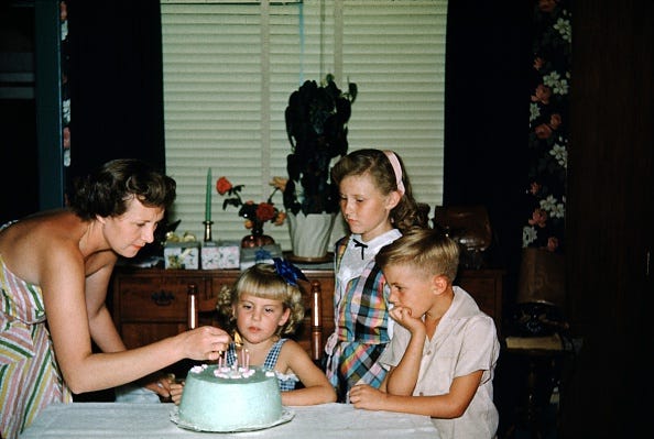 vintage birthday photos mother leaning over a table and lighting candles on a cake for a young childs birthday party, her brother and sister looking on, 1965. (photo by smith collection/gado/getty images).