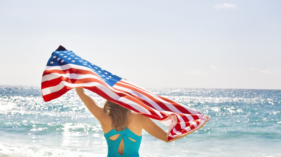 a young woman waving the us flag on a tropical beach vacation on fourth of july the national banner is displayed for the fourth of july, memorial day, and other national holidays and events photographed in horizontal format with copy space on location in kauai, hawaii, usa