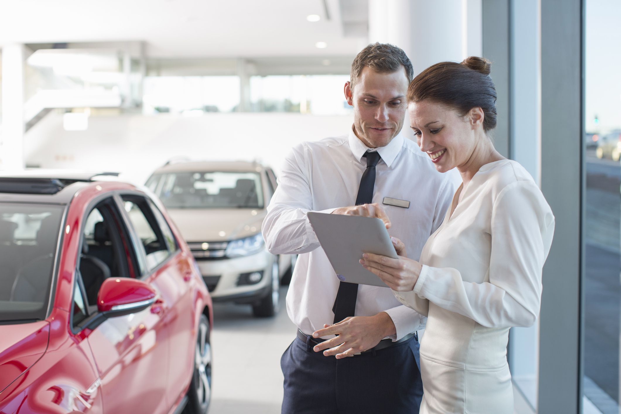 salesman and female customer using digital tablet in car dealership