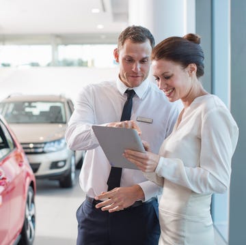 salesman and female customer using digital tablet in car dealership