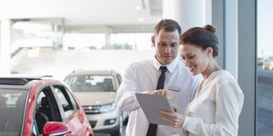 salesman and female customer using digital tablet in car dealership