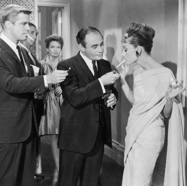 1961, american actors george peppard and martin balsam compete to light belgian born actor audrey hepburns cigarette at a formal party in a still from director blake edwards film, breakfast at tiffanys photo by paramount picturesgetty images