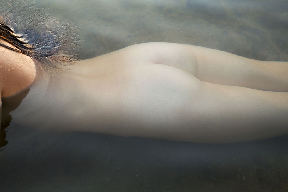 nude young woman laying on her stomach in a pond submerged by water, cropped from above