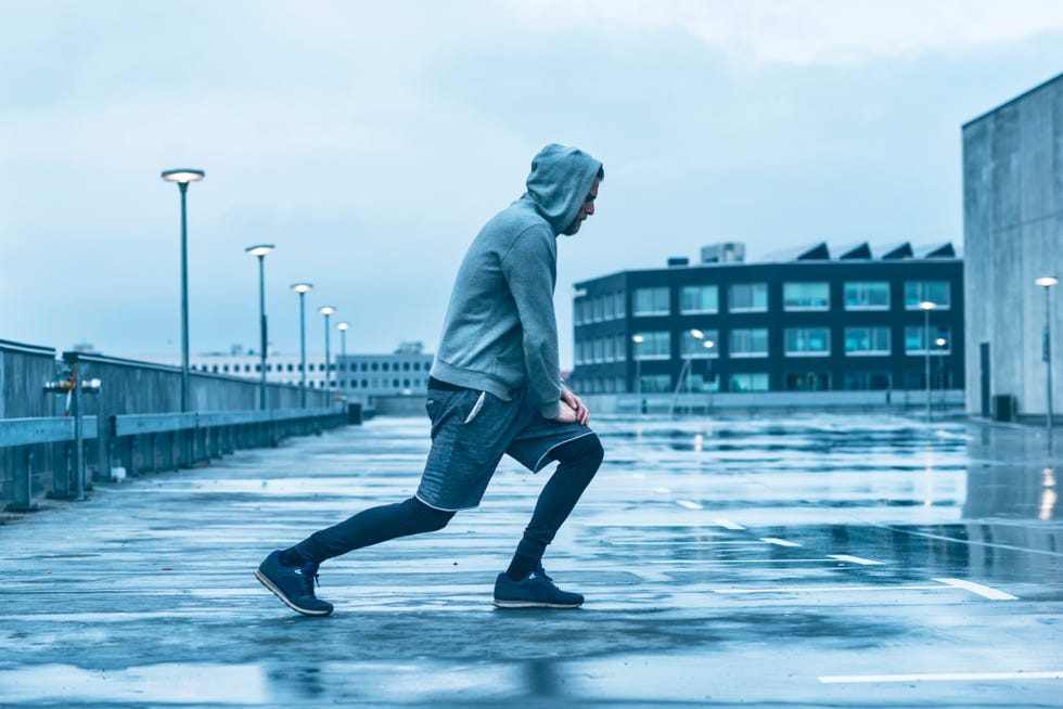 male runner wears sports clothes and stretches his leg he prepares to go running outside in the rain