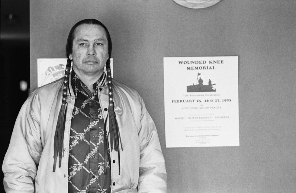 Russell Means een van de leiders van de American Indianbeweging staat naast een poster voor een herdenking van Wounded Knee met onder meer een mars van drie dagen