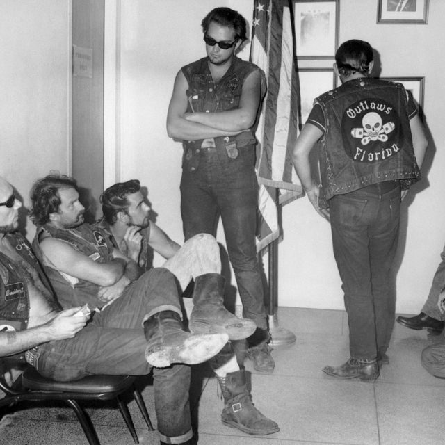 members of the outlaws motorcycle club sitting in chairs and standing inside a police waiting room