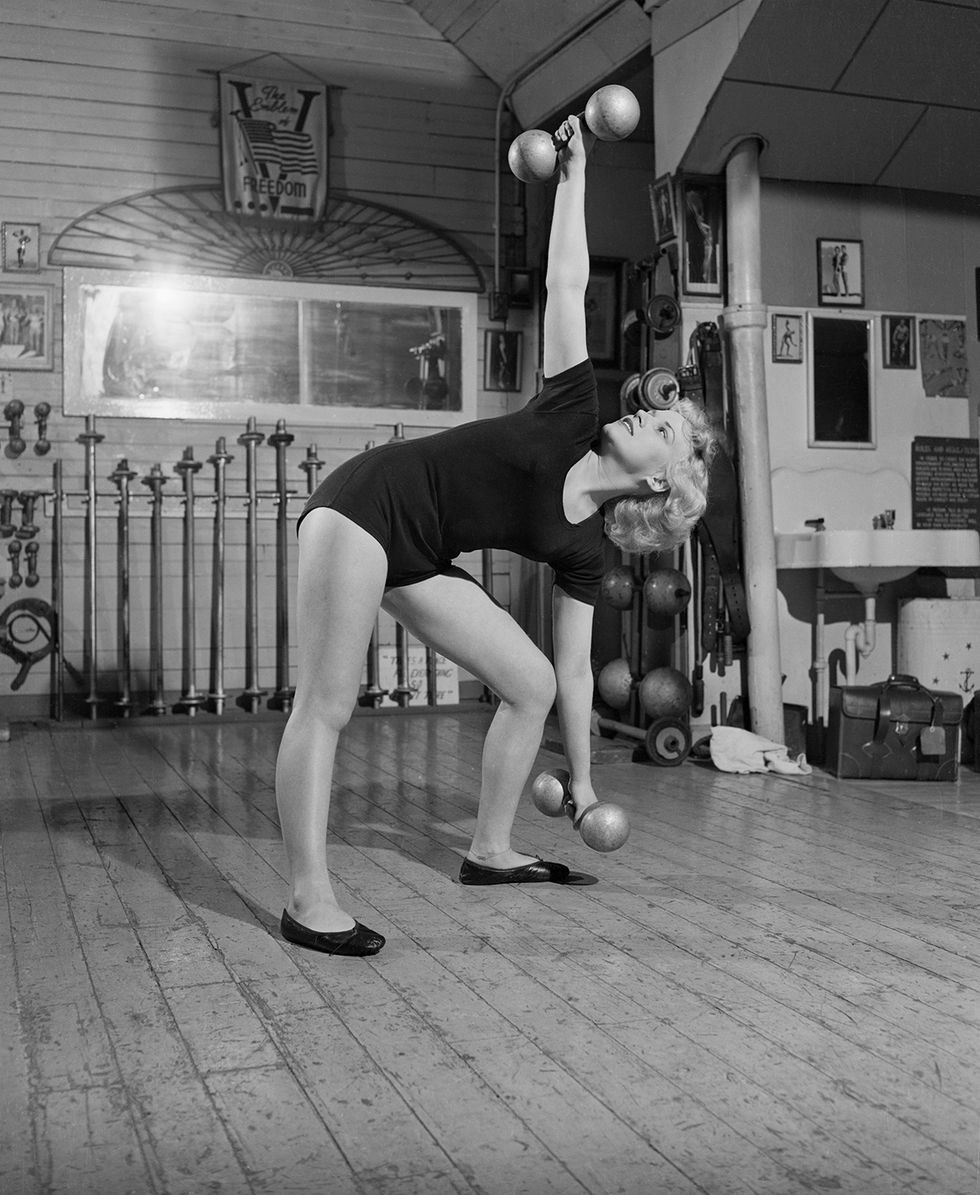 a black and white photograph of a woman in a leotard lifting weights
