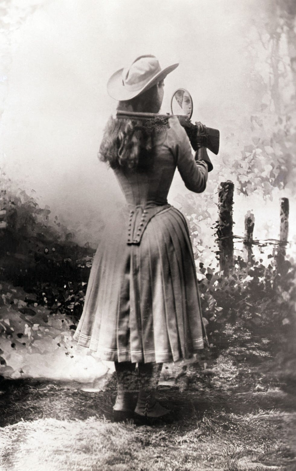 Oakley schiet met een geweer over haar schouder met behulp van een handspiegel De foto is gemaakt rond 1885 Dit was een van haar favoriete trucs en ze maakte vaak indruk op de toeschouwers Ze was al op jonge leeftijd bedreven met geweren nadat ze er voor het eerst een had opgepakt om voor haar familie te gaan jagen