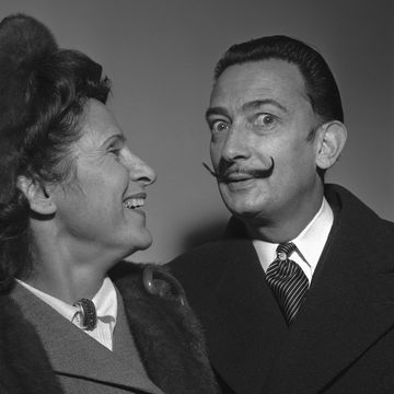 Modernistic artist Salvador Dali amuses his wife, Gala, with a display of his handlebar moustache. The painter-writer and spouse arrived in New York, Dec. 29, aboard the Vulcania. Dali recently completed three paintings in Italy and a book in Spain.
