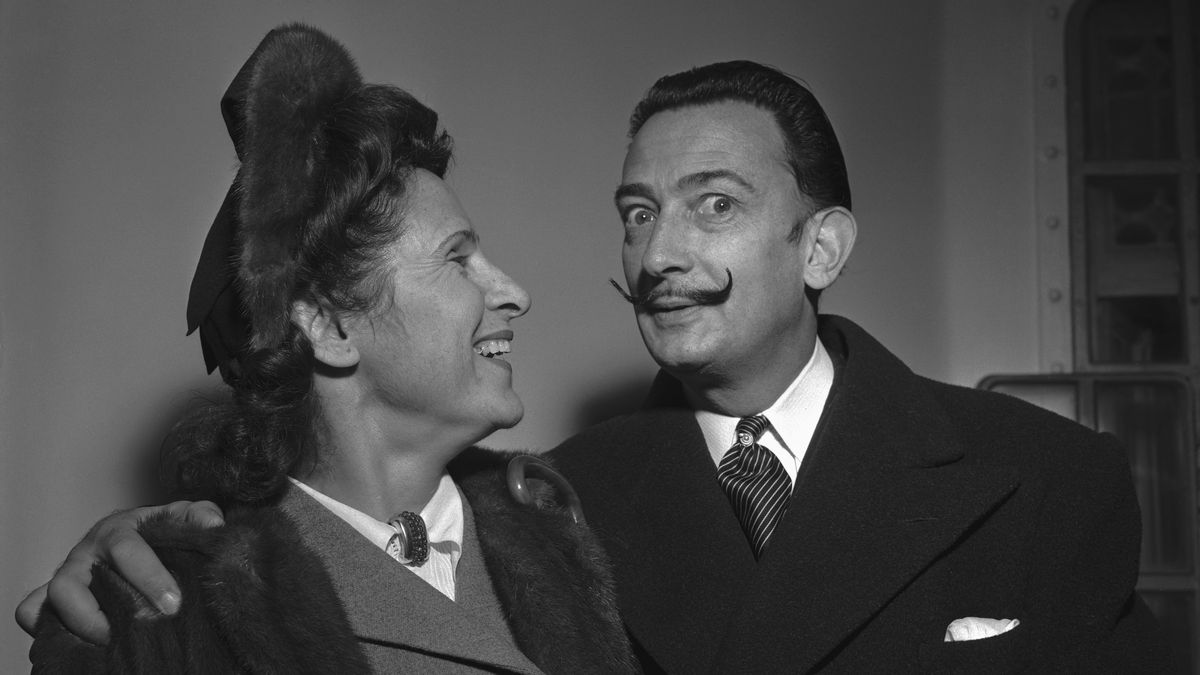 Modernistic artist Salvador Dali amuses his wife, Gala, with a display of his handlebar moustache. The painter-writer and spouse arrived in New York, Dec. 29, aboard the Vulcania. Dali recently completed three paintings in Italy and a book in Spain.