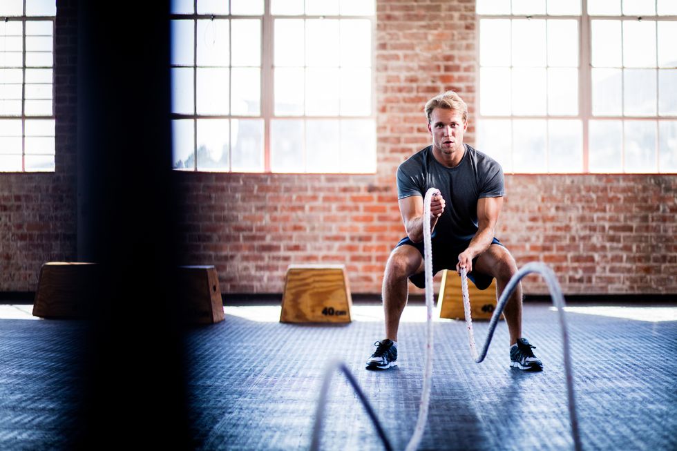 athletic young adult caucasian man doing battle ropes exercise during a gym training at the gym