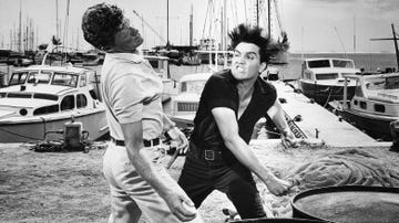 With his hair standing on end, and a nasty snarl, Elvis Presley proves he can belt a man just as much as he can belt a real tune. The mean blow clipped Jeremy Slate, in a scene from Hal Wallis's "Girls! Girls! Girls!", a musical from Paramount. Presley, the singing hero in the fil, takes apart Slate for trying to steal his girl, Laurel Goodwin.
