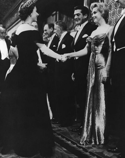 original caption queen elizabeth ii of england offers a gloved hand to hollywood glamour girl marilyn monroe miller during the queen's visit with celebrities at the royal film performance standing beside marilyn is actor victor mature