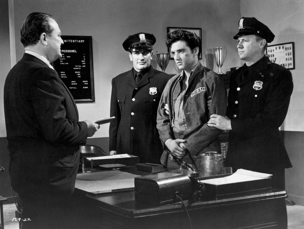 Elvis Presley is held by guards Carl Sax (left) and Hubi Kearns (right) as Warden Hugh Sanders prepares to sentence Elvis for creating a disturbance in prison in a scene from the 1957 film Jailhouse Rock.
