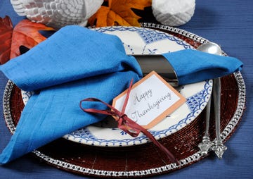 vintage style happy thanksgiving dining table place setting with vintage plate and dark blue napkin with turkey tureen on dark blue cheesecloth tablecloth closeup