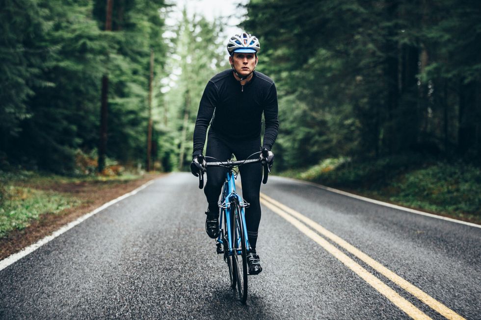 a man cycling in a beautiful oregon state forest setting on the road to larch mountain  he has a bright blue street bike that stands out from the green of the surrounding trees  he looks up the road ahead as he pedals hard uphill