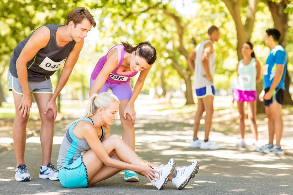 full length of marathon runner suffering from twisted ankle while competitors consoling her on street horizontal shot