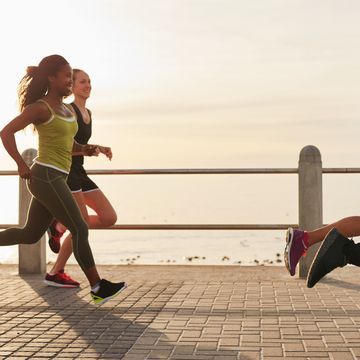 young woman running with friends on seaside promenade at the sunset fit young people doing running workout outdoors by along the sea