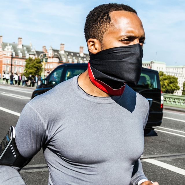 man in face mask running next to a street