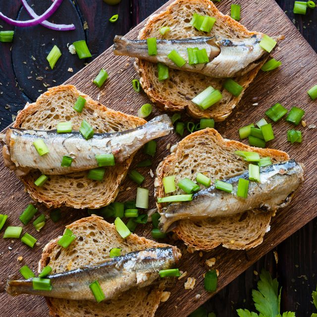 sandwich with sardines, sprinkle with onions on a cutting board on a black background with fennel and red onion
