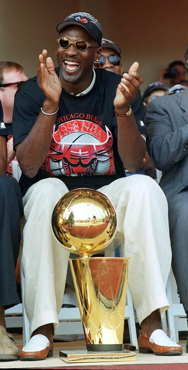 chicago, il   june 16  chicago bulls player michael jordan applauds as he sits with one of the teams six nba championship trophies he has helped the bulls win in the past eight seasons during the teams championship rally in chicago, il 16 june the bulls defeated the utah jazz four games to two in the nba finals to win their third straight nba title  photo credit should read peter pawinskiafp via getty images