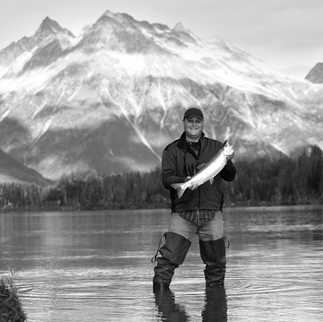 man holding up a fish he caught fishing on a secluded lake in alaska, silver salmon
