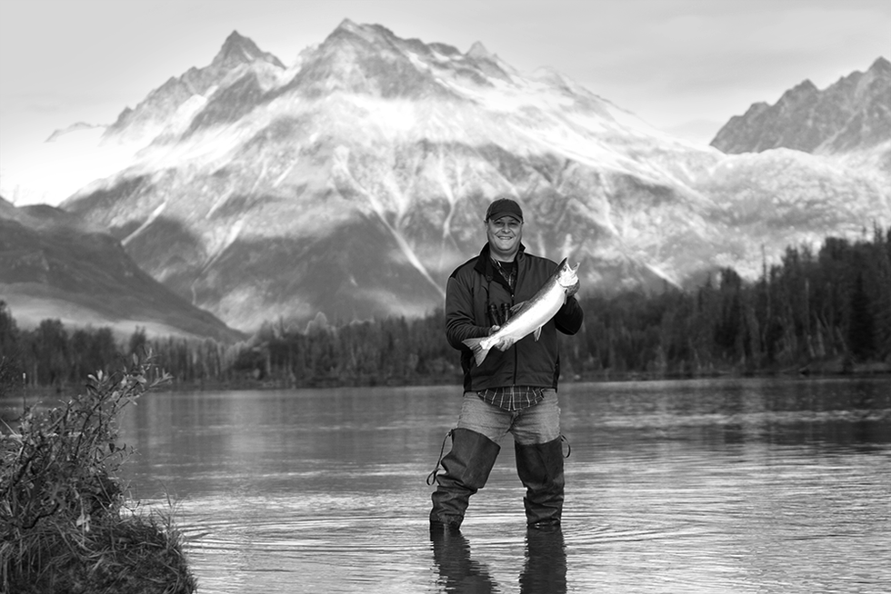 man holding up a fish he caught fishing on a secluded lake in alaska, silver salmon