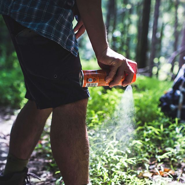 man spraying deet on legs while hiking