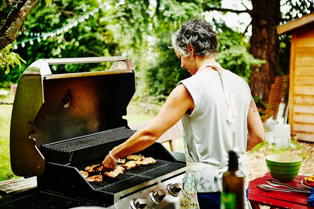 smiling woman grilling chicken on backyard barbecue on summer evening