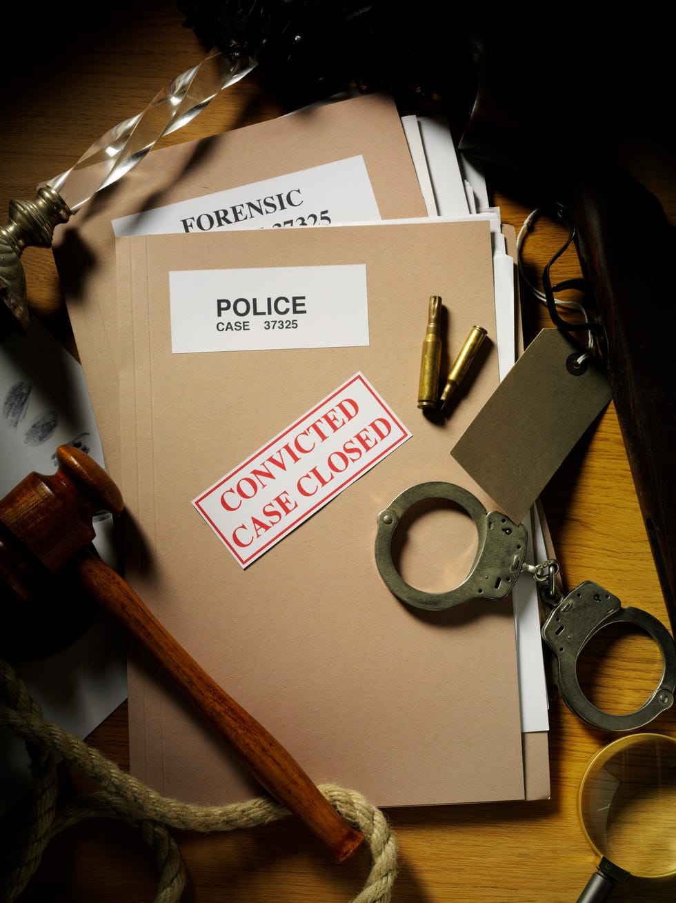 police handcuffs, shot gun and bullets with a candlestick as evidence framing a police case file with a gavel on a desk