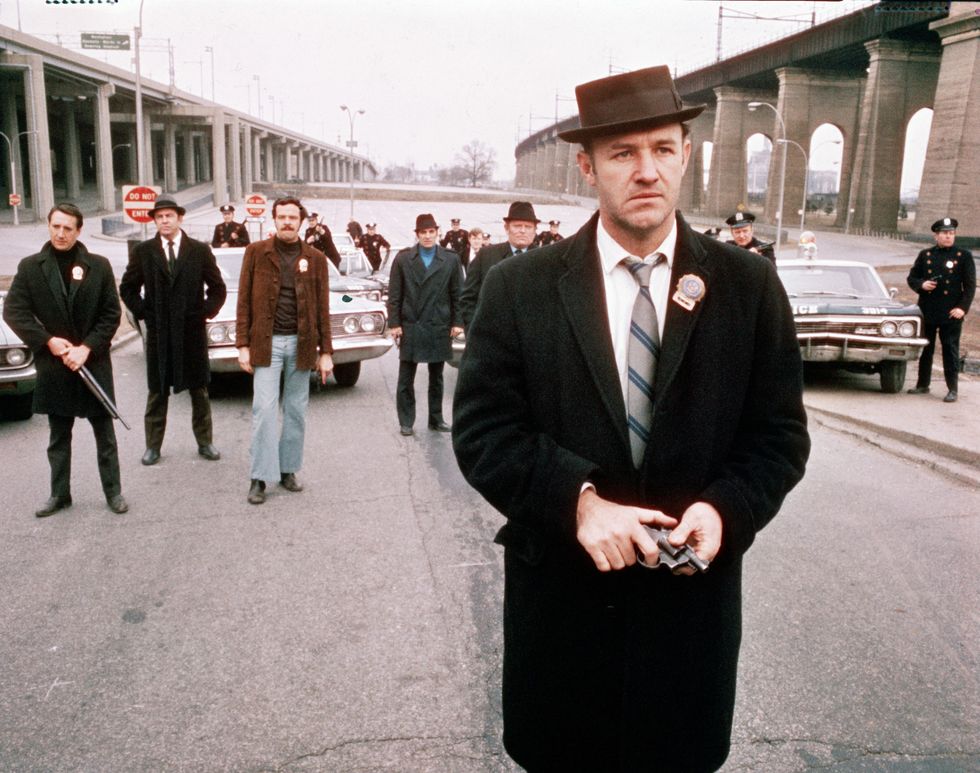 american actor gene hackman foreground, as detective jimmy 'popeye' doyle, stands in the street by an overpass in front of a group of policemen and holds a gun in his hands in a still from the film 'the french connection,' directed by william friedkin, 1971 in the background is actor roy scheider first from left as detective buddy 'cloudy' russo and policeman and actor eddie egan 1930   1995 fifth from left as walt simonson photo by 20th century foxhulton archivecourtesy of getty images