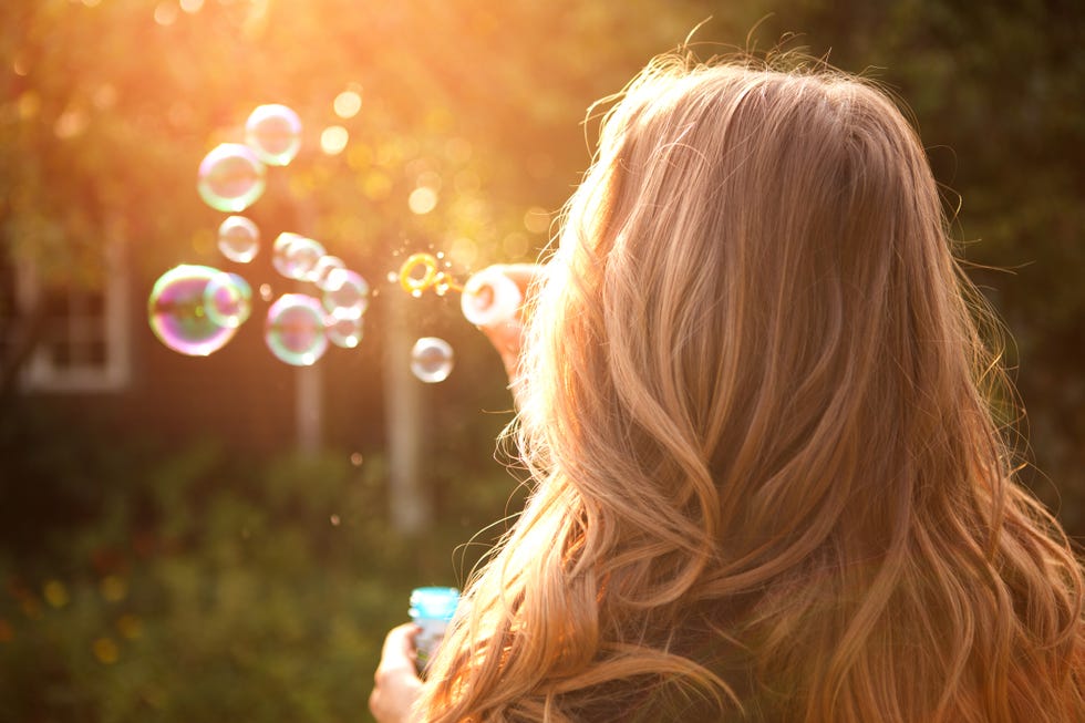 woman enjoying the sun outdoors in sunset, blowing soap bubbles 