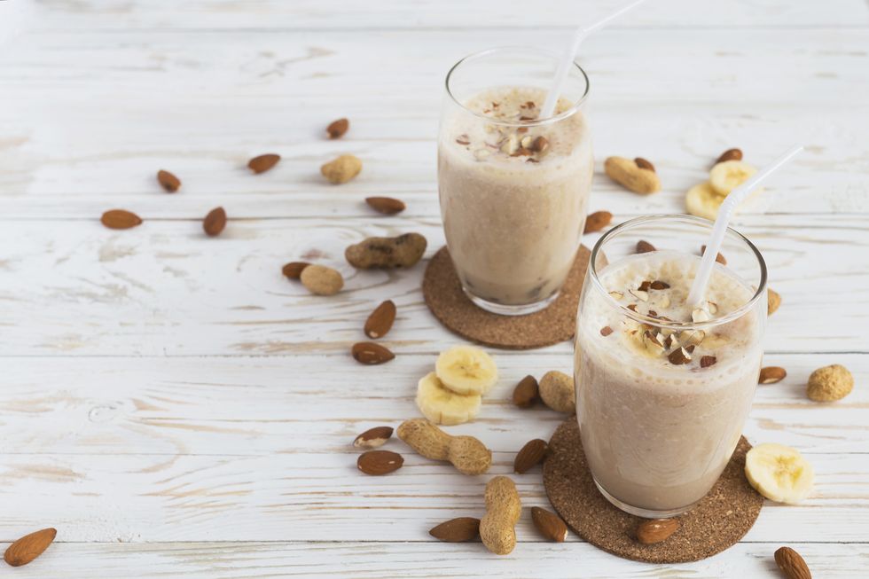 peanut and almond butter banana oat smoothie with paper straws on a wooden rustic table