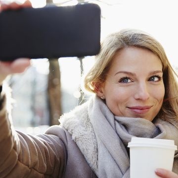 een blonde vrouw met een beker koffie in haar hand neemt een selfie