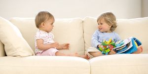 Baby girl (9-12 months) looking at toddler boy (12-15 months) on sofa with toys, side view